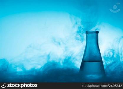 Chemical glass test tube with liquid and steam or smoke backlight on blue background with copy space