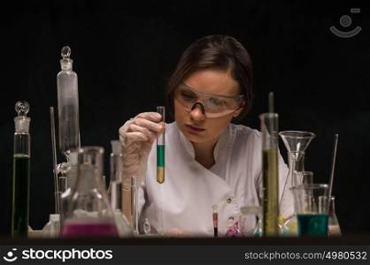 Chemical laboratory scene: attractive young PhD student scientist observing the tube with liquid
