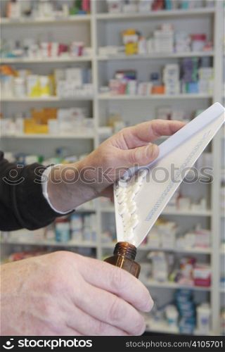 Chemist dispensing pills into a brown bottle with his hands