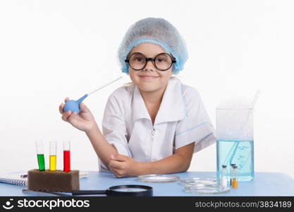 Chemist girl sitting at the table with the reagents in chemistry class and puts experiments