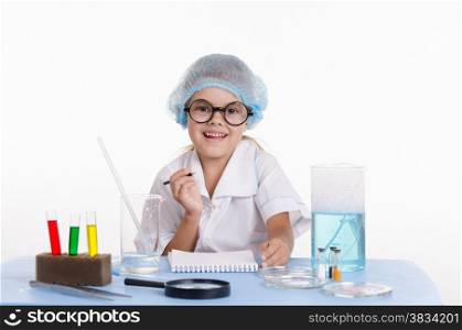 Chemist girl sitting at the table with the reagents in chemistry class and puts experiments