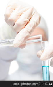 Chemist hands in rubber gloves pour hazardous liquids into test tubes close-up