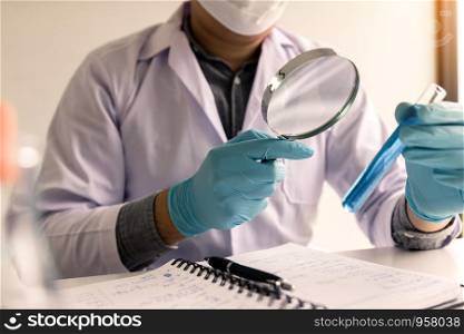 Chemist or scientist using magnifying glass looking the solution in test tube.