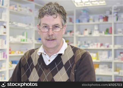chemist standing at counter in front of pills in pharmacy