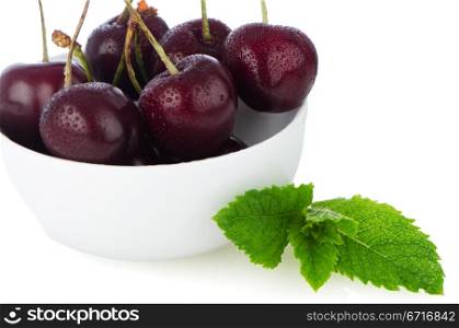 Cherries in white bowl on white reflective background.