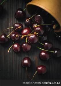 Cherries scattered from a mug on a dark wooden table. Scattered cherry from cup on black background.