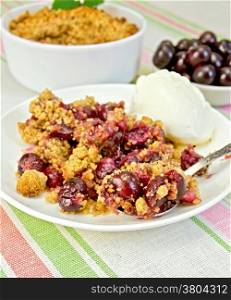 Cherry crumble in a white bowl and a plate with a spoon, cherries on a background of striped linen tablecloth