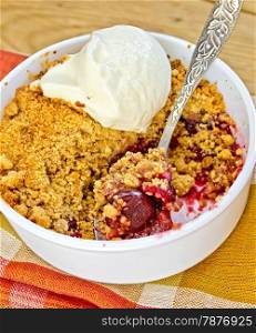 Cherry crumble in a white bowl with a spoon and ice cream on a checkered napkin on a wooden boards background