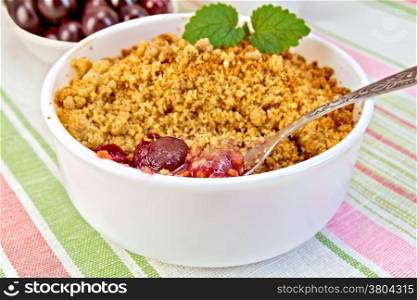 Cherry crumble in a white bowl with a spoon, cherries on a background of striped linen tablecloth