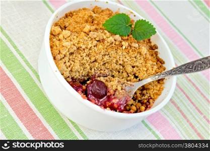 Cherry crumble in a white bowl with a spoon on a background of striped linen tablecloth