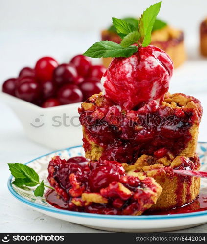 Cherry crumble pie decorated with a scoop of ice cream and drizzled with cherry sauce on a plate, white
