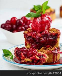 Cherry crumble pie decorated with a scoop of ice cream and drizzled with cherry sauce on a plate, white