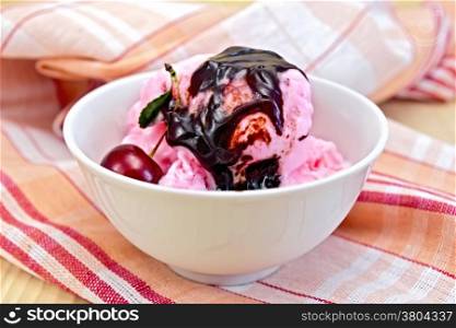 Cherry ice cream in a bowl with cherries and chocolate syrup on a napkin on the background of wooden boards