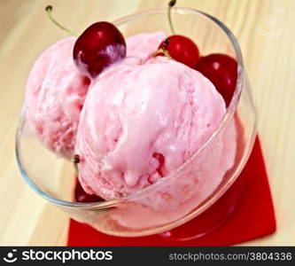 Cherry ice cream in a glass bowl on a red paper napkin on the background of wooden boards