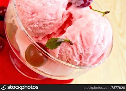 Cherry ice cream in a glass bowl with berries on red paper napkin on a wooden board