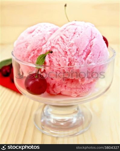 Cherry ice cream in a glass bowl with red tissue paper and berries on a background of wooden boards
