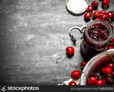 Cherry jam and metal tool for cherries. On a black wooden background.. Cherry jam and metal tool for cherries.