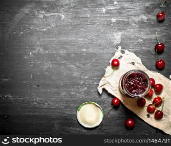 Cherry jam in a jar on the old fabric. On a black wooden background.. Cherry jam in a jar on the old fabric.
