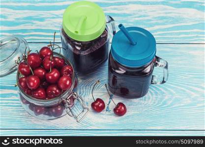Cherry juice with glass of berries. Cherry juice with glass jar of berries on blue wooden background