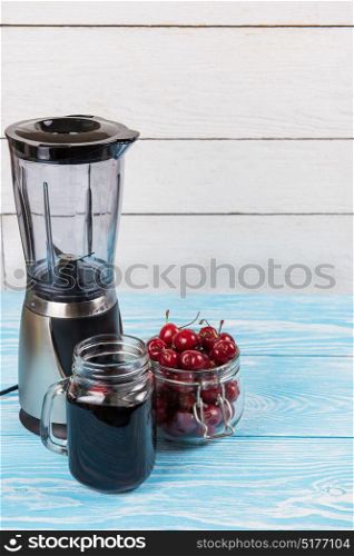 Cherry juice with glass of berries. Cherry juice with glass jar,of berries, blender and juice on blue wooden background