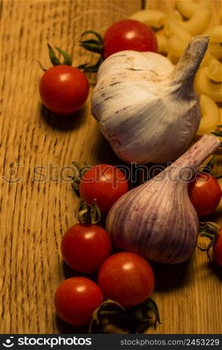 Cherry tomatoes, garlic and pasta on a wooden board. Food concept.