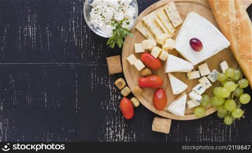 cherry tomatoes grapes cheese blocks baguette round chopping board textured backdrop