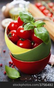 Cherry tomatoes in a bowl with basil and pasta ingredients on wooden background