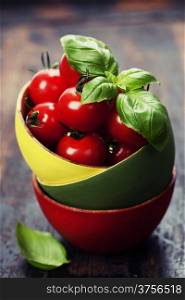 Cherry tomatoes in a bowl with basil over wood