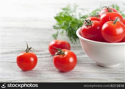 Cherry tomatoes in white dish and green dill on a wooden table