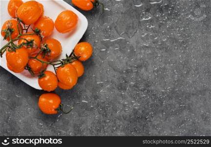 Cherry tomatoes of orange color in drops of water, layout on a gray table. Dark style, ingredients for salad or dish with vegetables. copy space for text