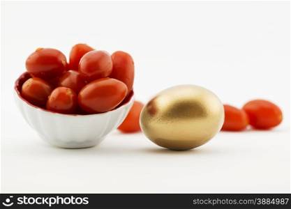 Cherry tomatoes placed with gold egg on white background with copy space available. Metaphors suggest fresh agriculture, local produce, farm industry, restaurant business, ogranic foods, are successful investments. Healthy diet and nutrition pay off.