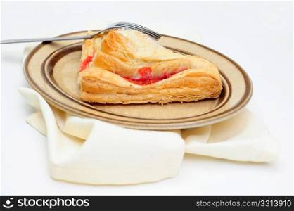 Cherry Turnover Side View. A sweet Cherry Turnover with course ground sugar on top served on an oval brown colored saucer with a light colored cloth napkin under the plate