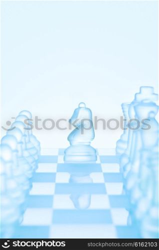 Chess game concept of an icy frosted chess knight standing among chess pieces on glacial chessboard ready for making an L-shaped move.
