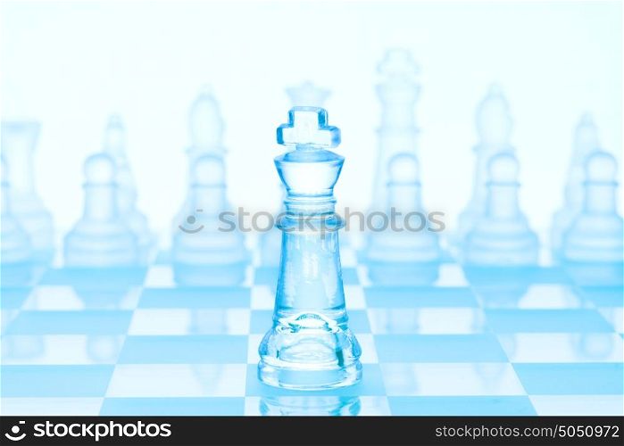 Chess game concept of an icy frosted king standing in front of chess pieces on glacial chessboard.