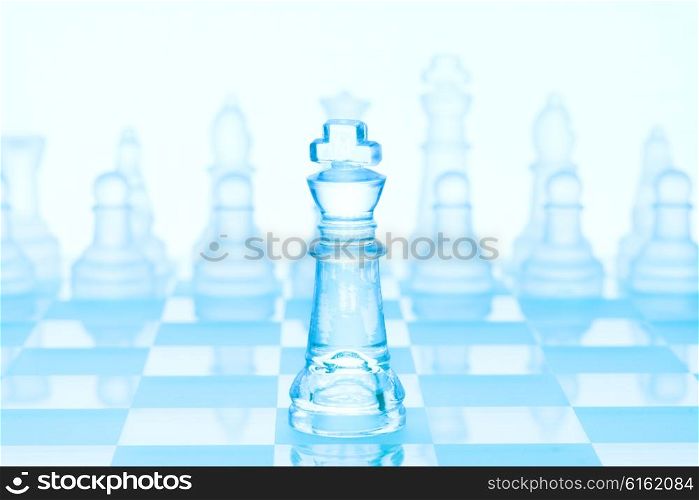 Chess game concept of an icy frosted king standing in front of chess pieces on glacial chessboard.