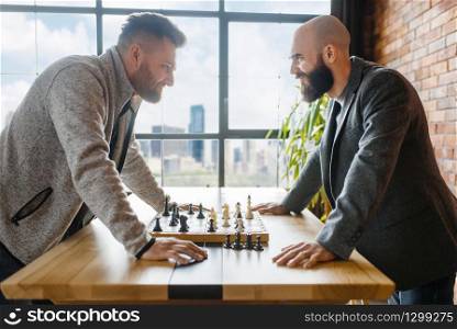 Chess players look into each other&rsquo;s eyes. Two chessplayers finished intellectual tournament indoors. Chessboard on wooden table
