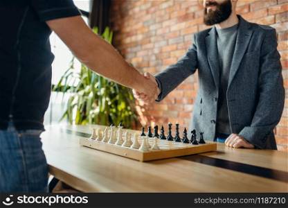 Chess players shake hands before the game. Two male chessplayers begin the intellectual battle indoors.. Chess players shake hands before the game