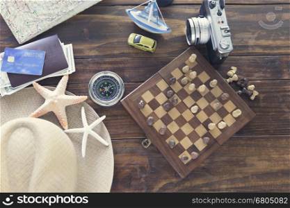 chessboard, hat, compass, passport, credit card, banknote money, camera, map, car ship and starfish figurine on wooden table for use as traveling concept (vintage tone and selected focus)