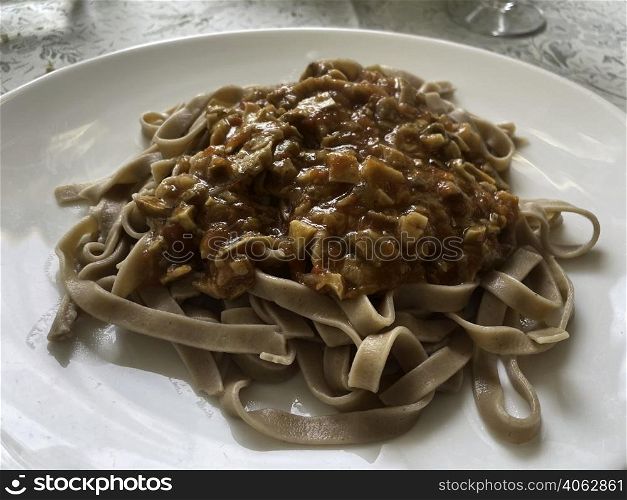Chestnut flour pasta with mushroom sauce on a white plate. Natural light