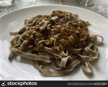Chestnut flour pasta with mushroom sauce on a white plate. Natural light
