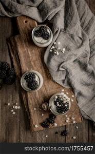 Chia pudding with blackberries, three portions in glass jars on a dark table.
