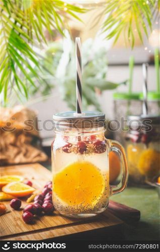Chia seeds detox water with orange fruit slice , lemon juice and cranberries in glass jar with drinking straw on kitchen table with ingredients. Summer drinks concept. Fitness and diet nutrition