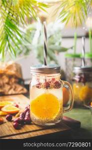 Chia seeds detox water with orange fruit slice , lemon juice and cranberries in glass jar with drinking straw on kitchen table with ingredients. Summer drinks concept. Fitness and diet nutrition