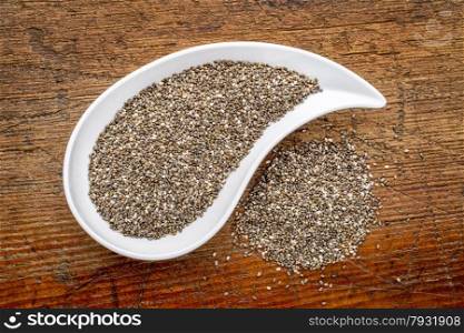 chia seeds in a teardrop shaped bowl - top view against rustic wood