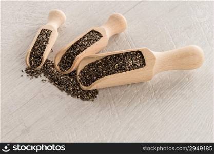 Chia seeds in wooden scoops on wooden table.