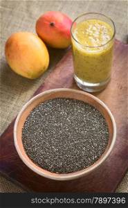 Chia seeds (lat. Salvia hispanica) in ceramic bowl with mango and chia juice in the back photographed with natural light. Chia seeds are considered a superfood containing proteins, omega fats, minerals and antioxidants. (Selective Focus, Focus in the middle of the bowl and the front rim of the glass)