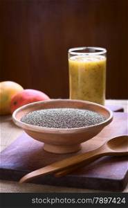Chia seeds (lat. Salvia hispanica) in clay bowl with mango and chia juice in the back photographed with natural light. Chia seeds are considered a superfood containing proteins, omega fats, minerals and antioxidants. (Selective Focus, Focus one third into the bowl)