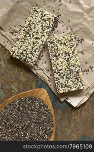 Chia seeds (lat. Salvia hispanica) on small bamboo plate with chia-sesame-honey granola bar, photographed overhead on slate with natural light. Chia seeds are considered a superfood containing protein, omega fat, minerals, antioxidants.