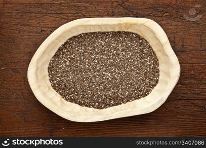 chia seeds (Salvia Hispanica) in a rustic wood bowl against grunge dark wooden table surface, top view