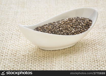 chia seeds (Salvia Hispanica) in a small white bowl against burlap canvas